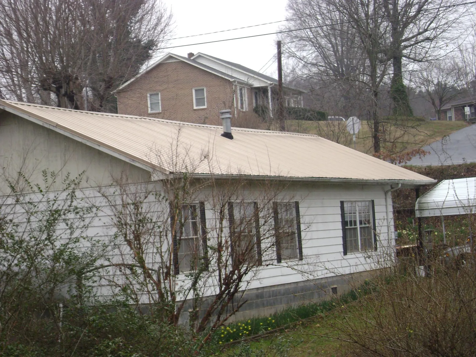 Tan metal roof on a white sided house set into a hillside — Commercial Roofing by Roofing Brothers in Gill