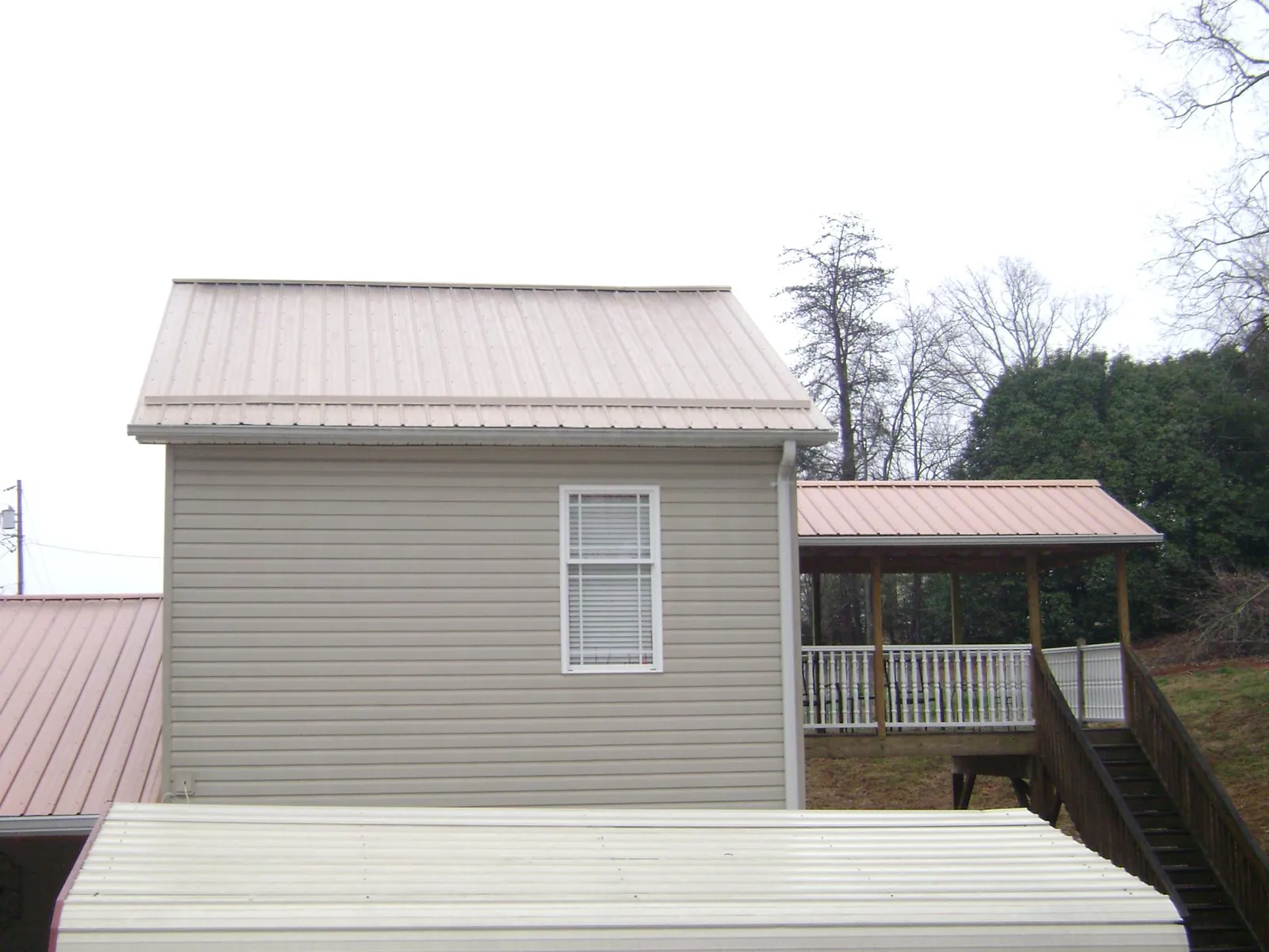 Tan metal roofs on a two story addition and attached porch, from a Roof Replacement job in Gill